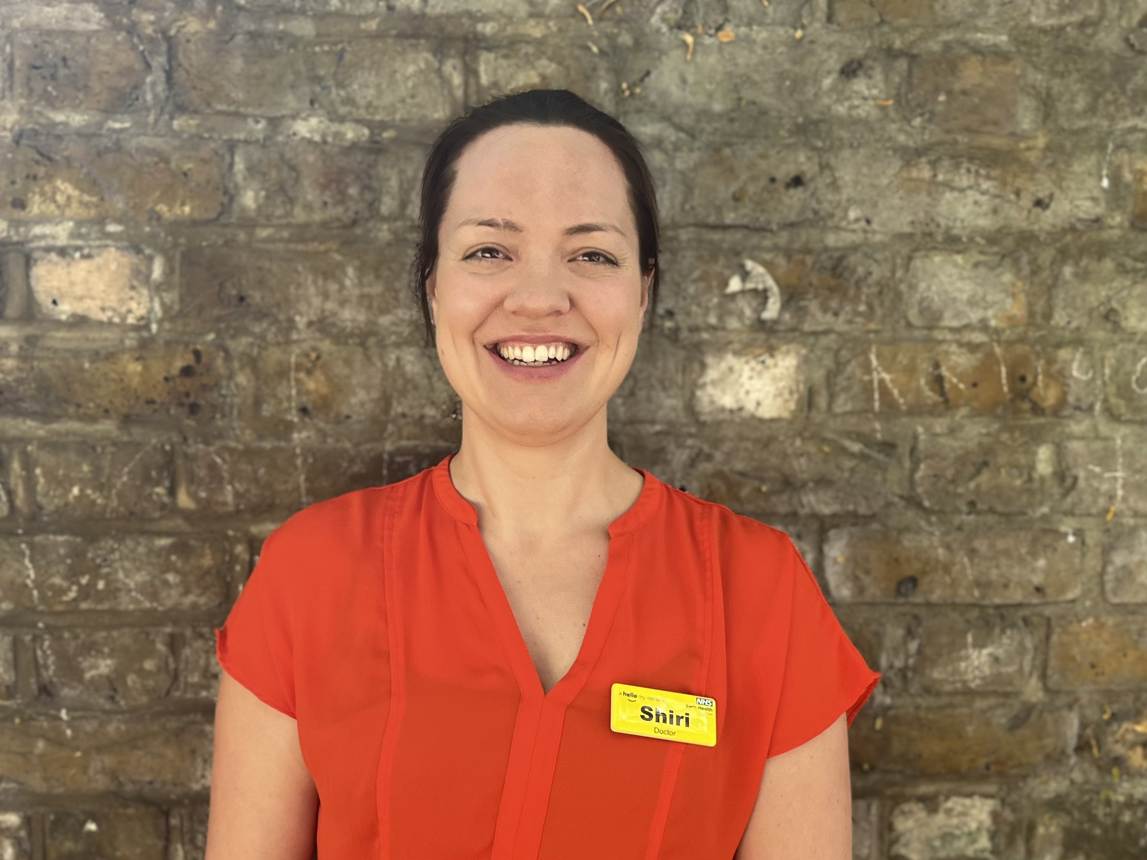 Dr Shiri Lejay wearing a red shirt and smiling at the camera